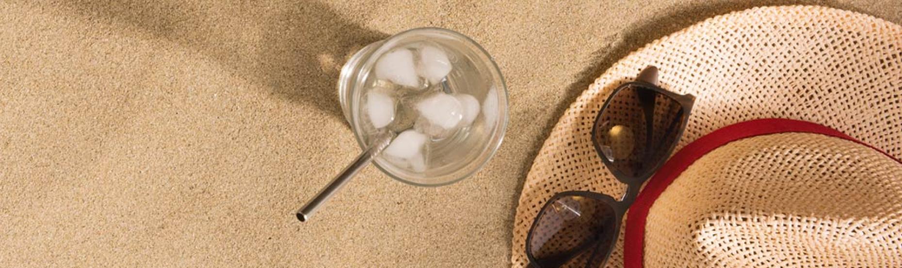 Warm sand, summer hat, sunglasses, icy drink, and seashells.